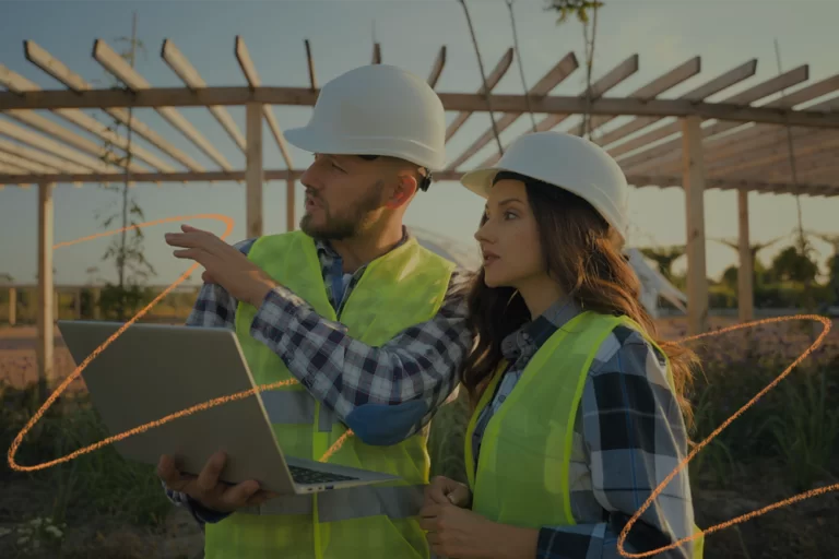 Dois profissionais da construção civil, usando capacetes e coletes refletivos, analisam um projeto em um notebook em meio a uma obra ao ar livre. A imagem ilustra a aplicação prática de anúncios digitais na construção civil, destacando como a tecnologia e o marketing estão cada vez mais presentes nas decisões estratégicas do setor.